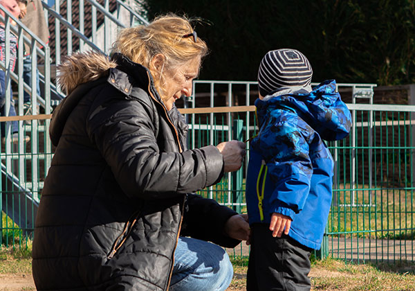 Übergang von der Kippe in die Kita im Kastanienhof Oldenburg, Erzieherin hilft Kind beim Ankleiden der Jacke auf dem Spielplatz