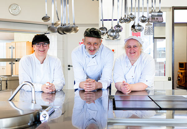 Küchenteam im Kastanienhof Oldenburg - drei Mitarbeiter stehen an Küchentresen der Schulküche